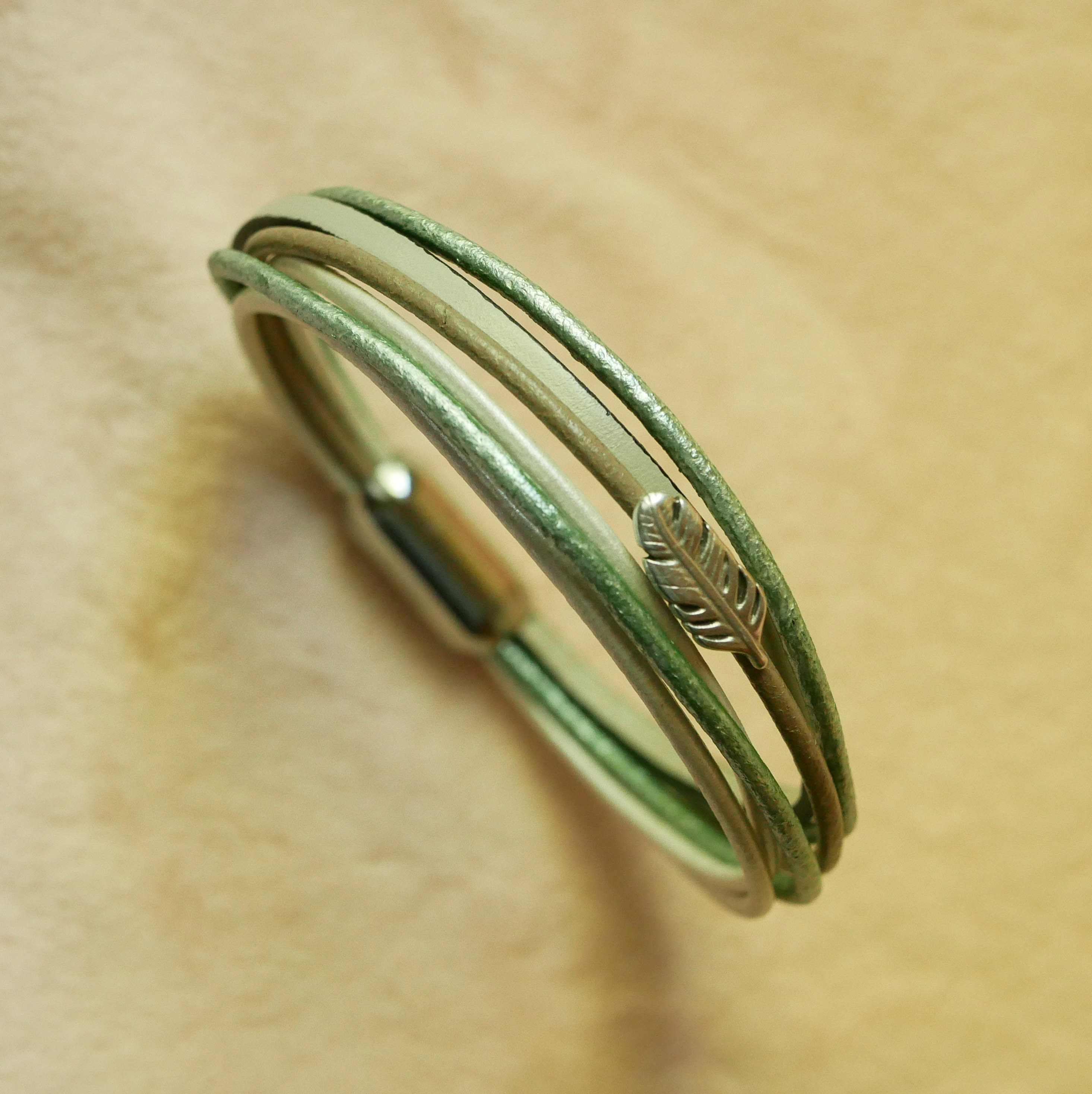 Pulsera multicuero en tonos beige, verde pálido y nacarado, decorada con una pequeña pluma