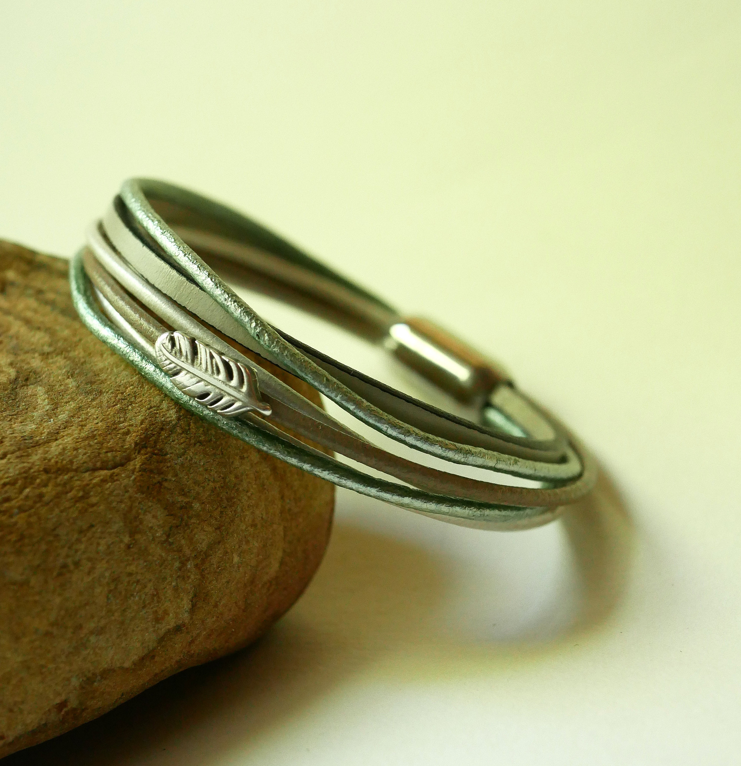 Pulsera multicuero en tonos beige, verde p&aacute;lido y nacarado, decorada con una peque&ntilde;a pluma