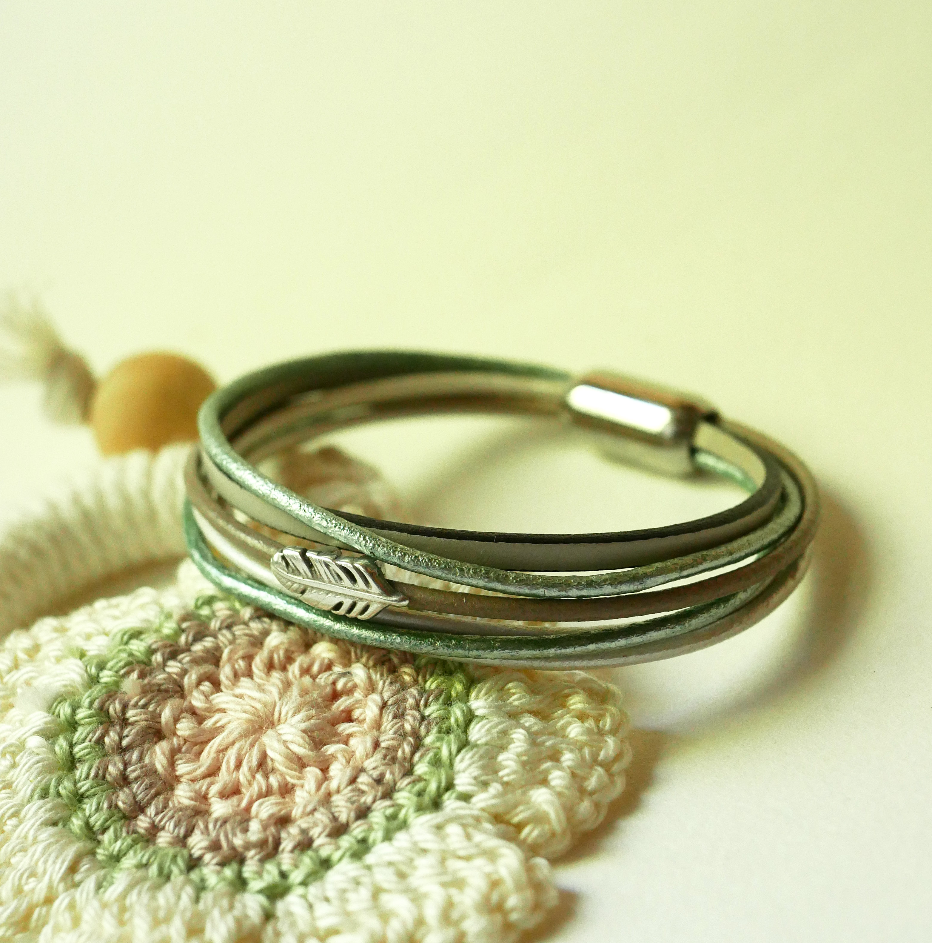 Pulsera multicuero en tonos beige, verde pálido y nacarado, decorada con una pequeña pluma