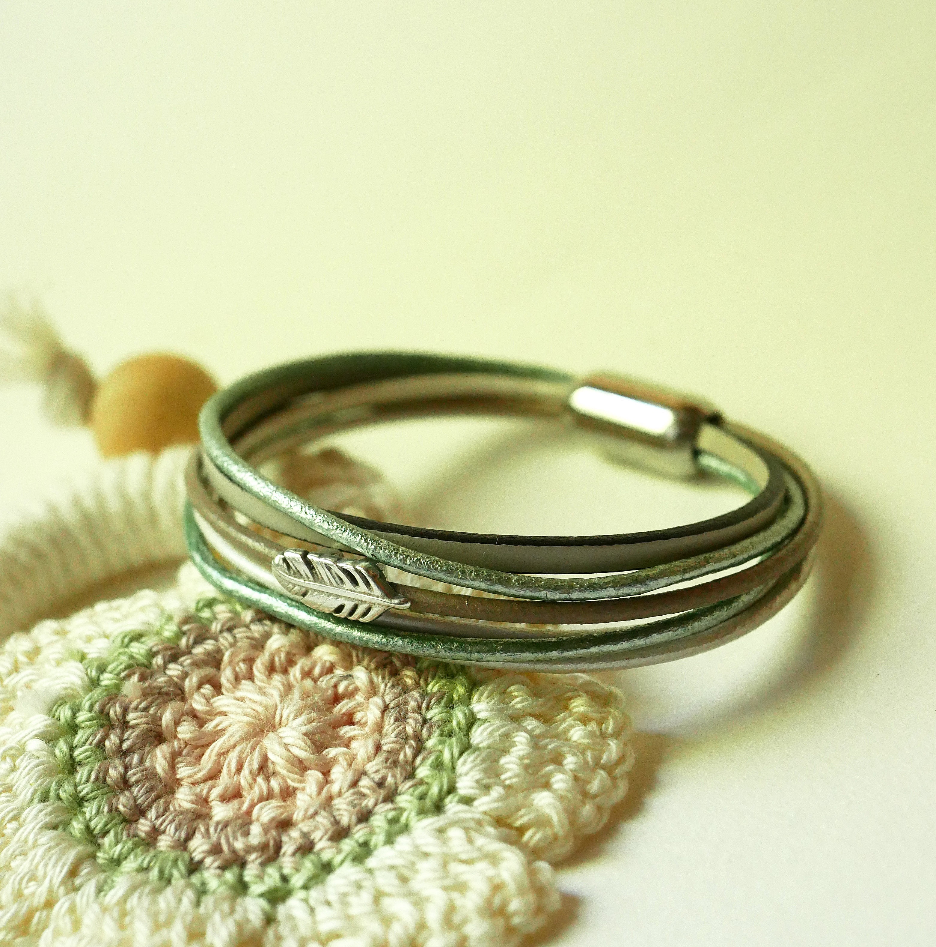 Pulsera multicuero en tonos beige, verde p&aacute;lido y nacarado, decorada con una peque&ntilde;a pluma