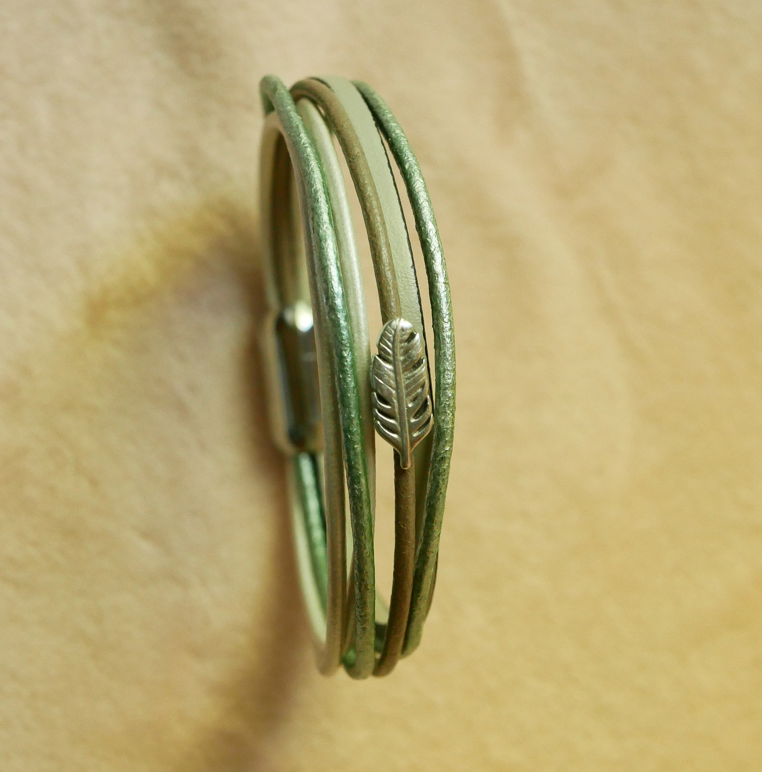 Pulsera multicuero en tonos beige, verde pálido y nacarado, decorada con una pequeña pluma