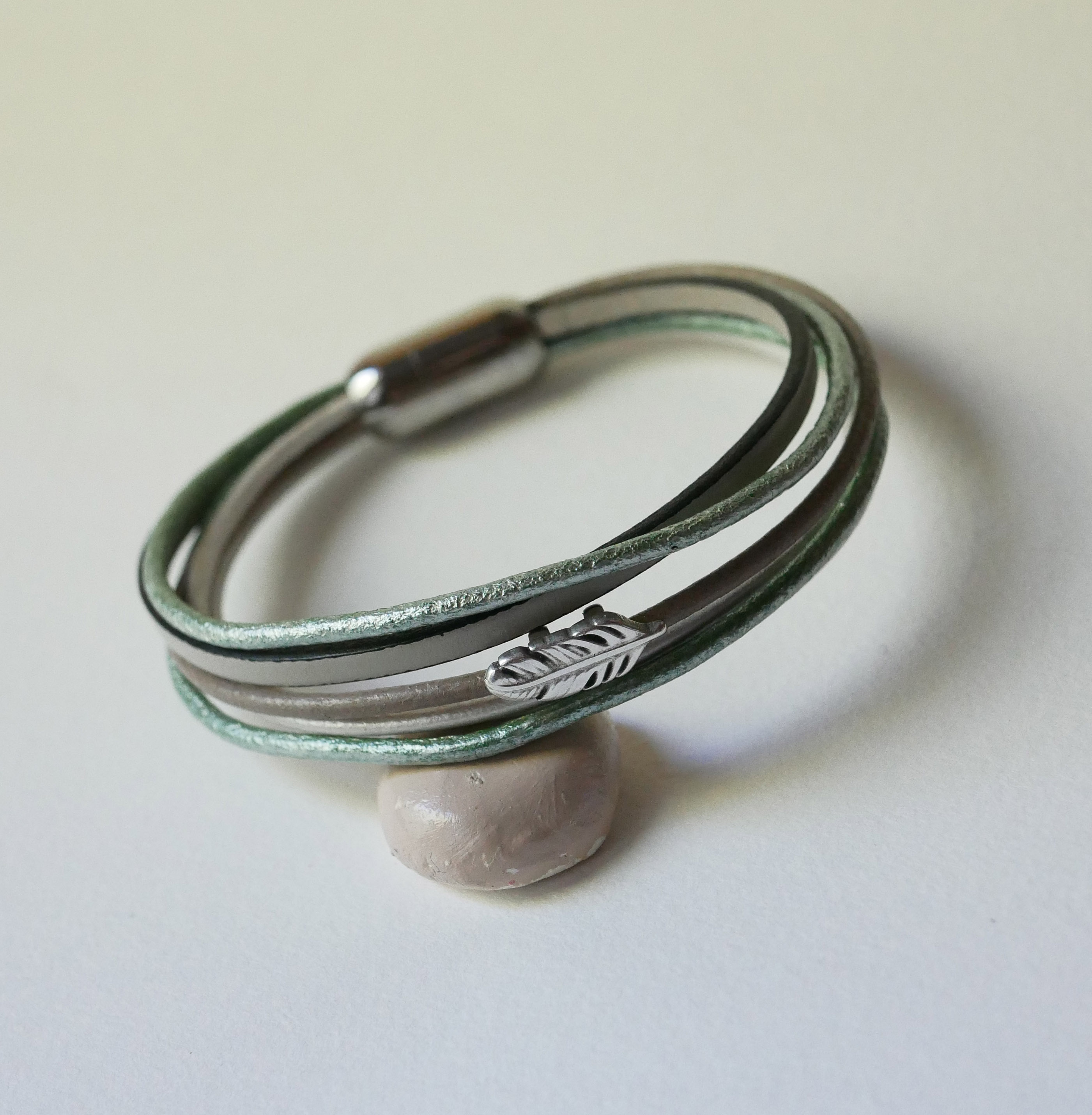 Pulsera multicuero en tonos beige, verde pálido y nacarado, decorada con una pequeña pluma