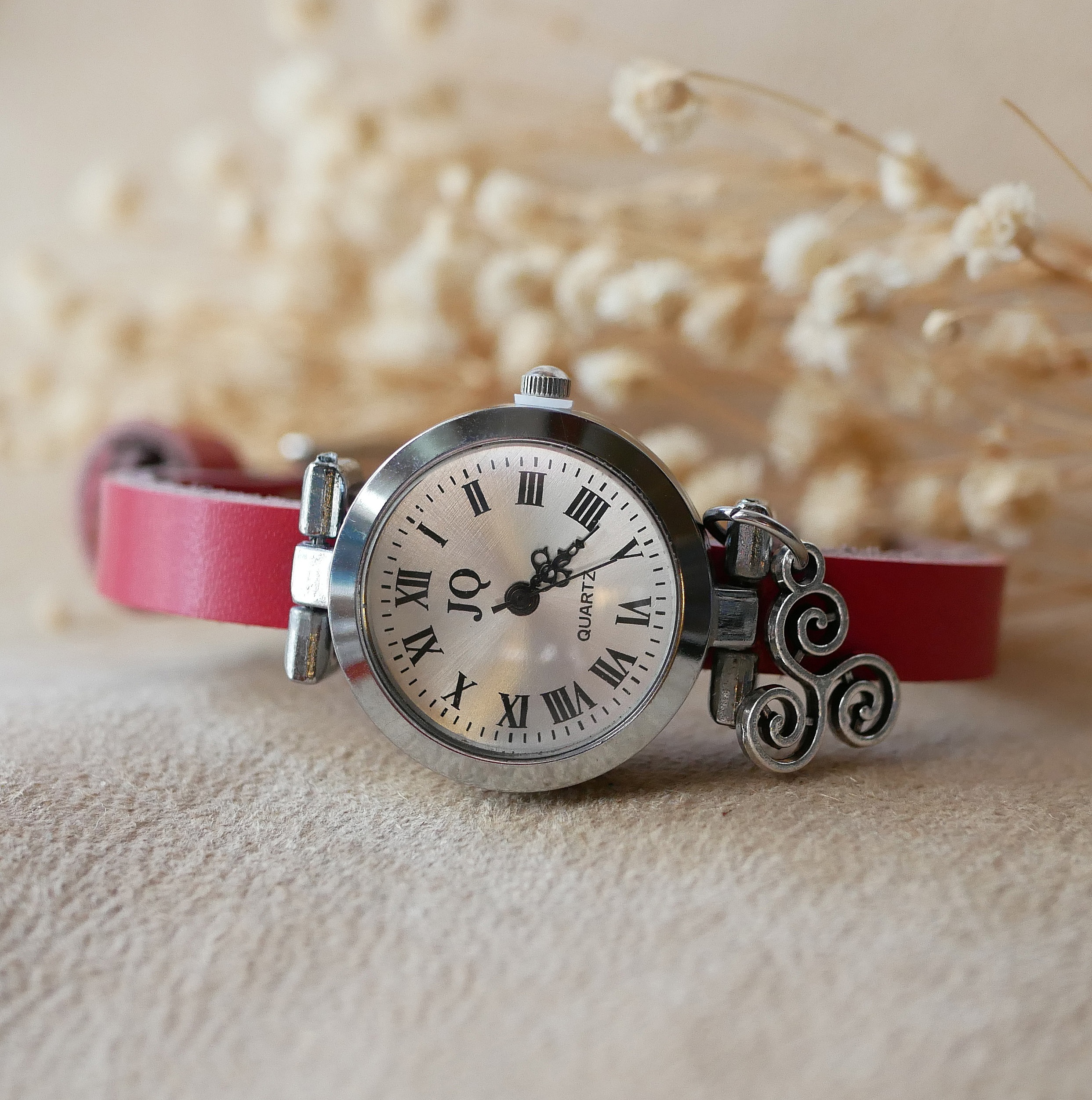 Montre argentée à bracelet cuir rouge avec breloque celtique.