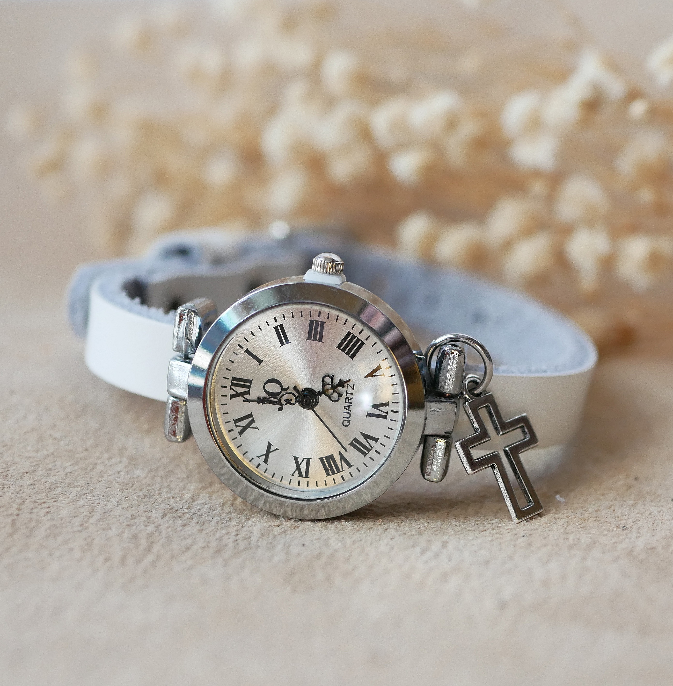 Montre argentée à bracelet cuir blanc avec breloque croix.