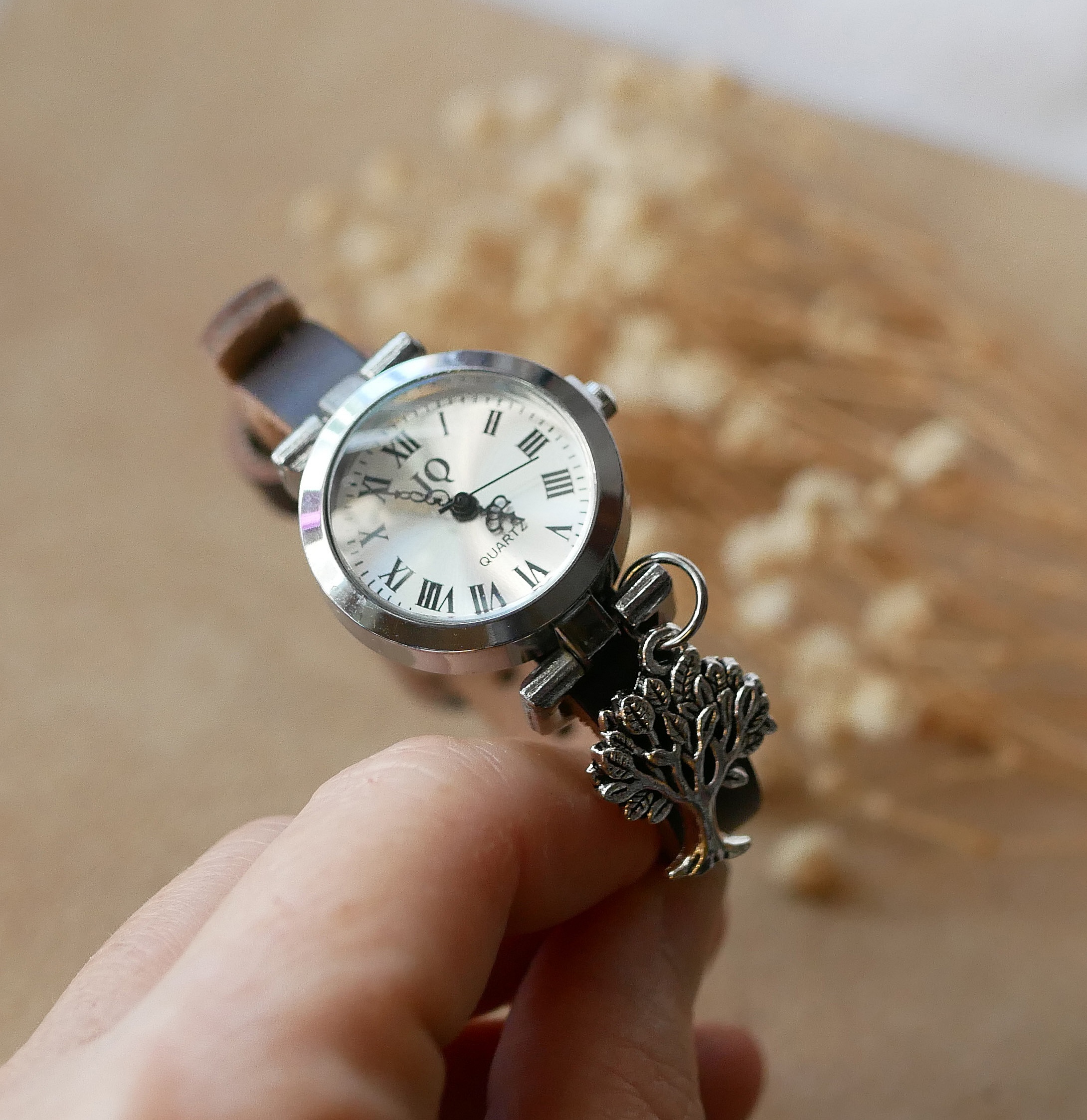 Montre argentée avec bracelet cuir et pendentif arbre.